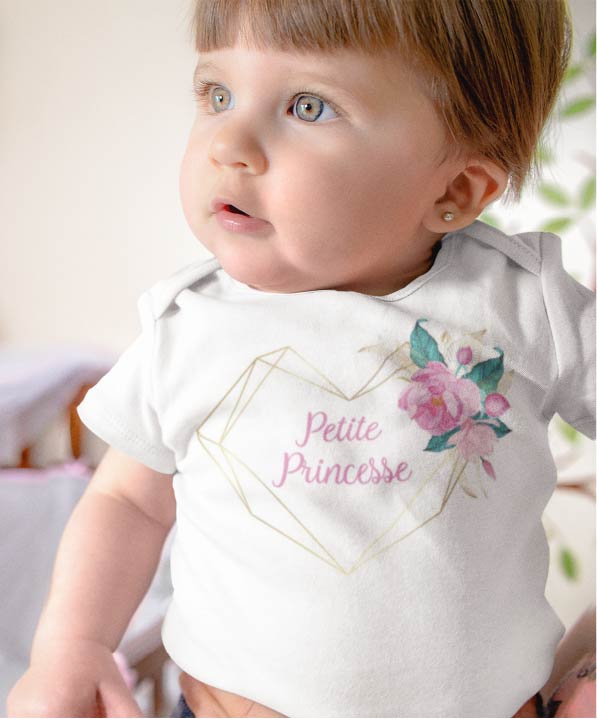 Sur cette image on peut voir un body personnalisé "Petite princesse" dans un cœur avec des fleurs. Il est imprimé au sein de notre boutique l'usine du t-shirt Caissargues dans le Gard.