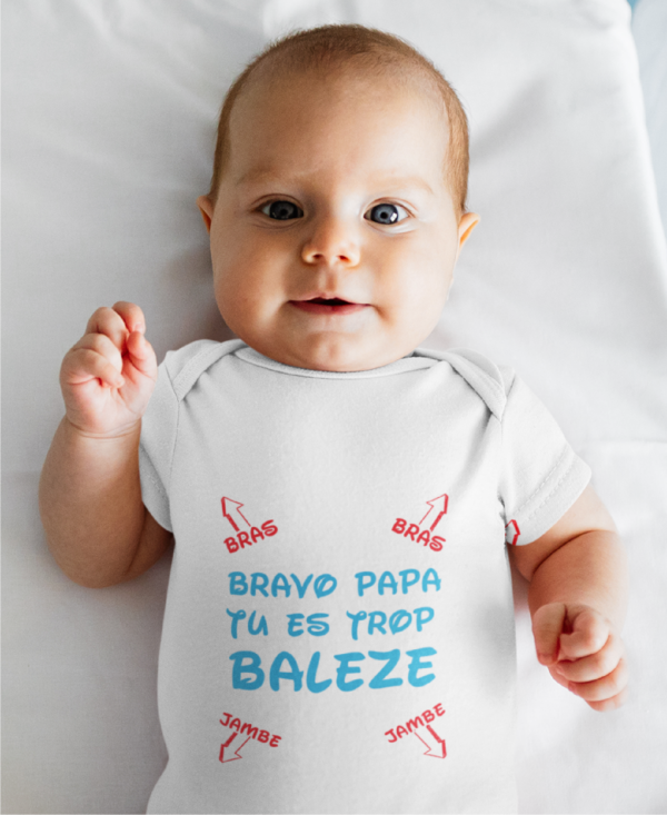 Sur cette image, on peut voir un body personnalisé "Bravo papa tu est trop balèze". C'est unbébé aux yeux bleu qui le porte. Ce body est personnalisé à Caissargues dans le Gard.