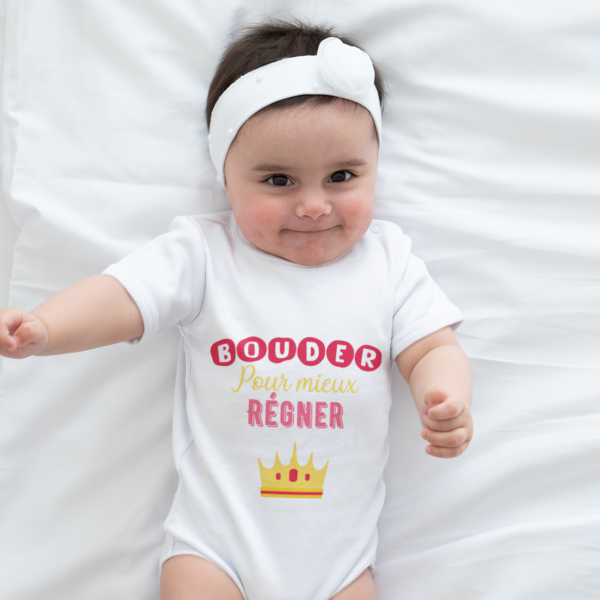 Sur cette image on peut voir un body bébé personnalisé "Bouder pour mieux régner" avec une petite couronne. Ce body bébé est imprimé au sein de notre boutique qui se trouve à Caissargues à coté de Nîmes dans Gard.