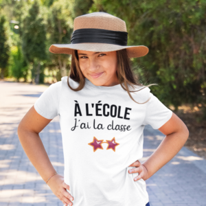 Sur cette image on peut voir un t-shirt enfant personnalisé "A l'école j'ai la classe" avec l'image d'une paire de lunettes de soleil. Il est imprimé au sain de notre boutique qui se trouve à Caissargues à coté de Nîmes dans le Gard.