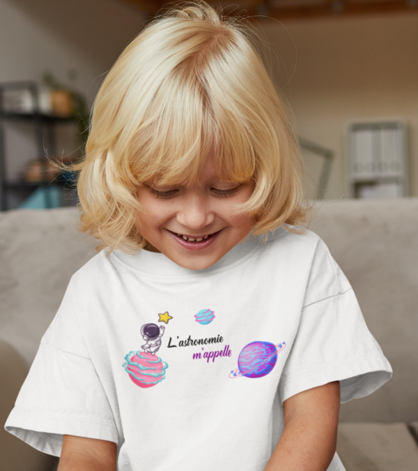 Sur cette image on peut voir un t-shirt enfant personnalisé "L'astronomie m'appelle" avec des images de planètes, étoiles et astronautes. Il est imprimé au sain de notre boutique qui se trouve à Caissargues à coté de Nîmes dans le Gard.